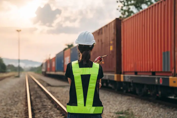 a female worker with a walkie talkie watching a train with shipping container move