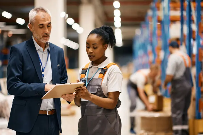 a mature manager reviewing a list with employee at a shipping warehouse