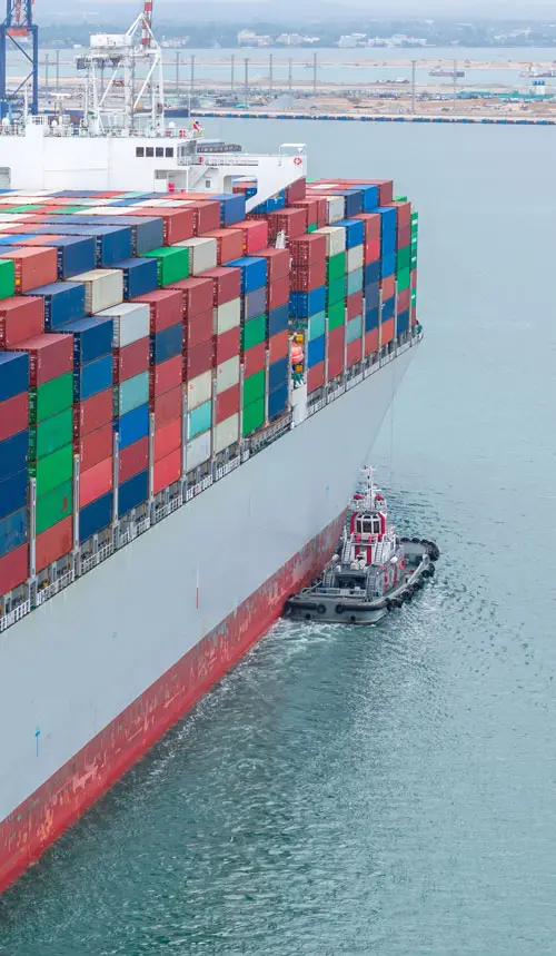 a container ship being shepherd to port by smaller boat