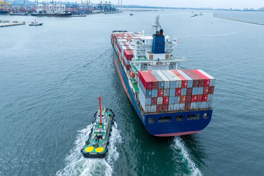 a loaded cargo ship getting close to port and is being guided by a smaller boat